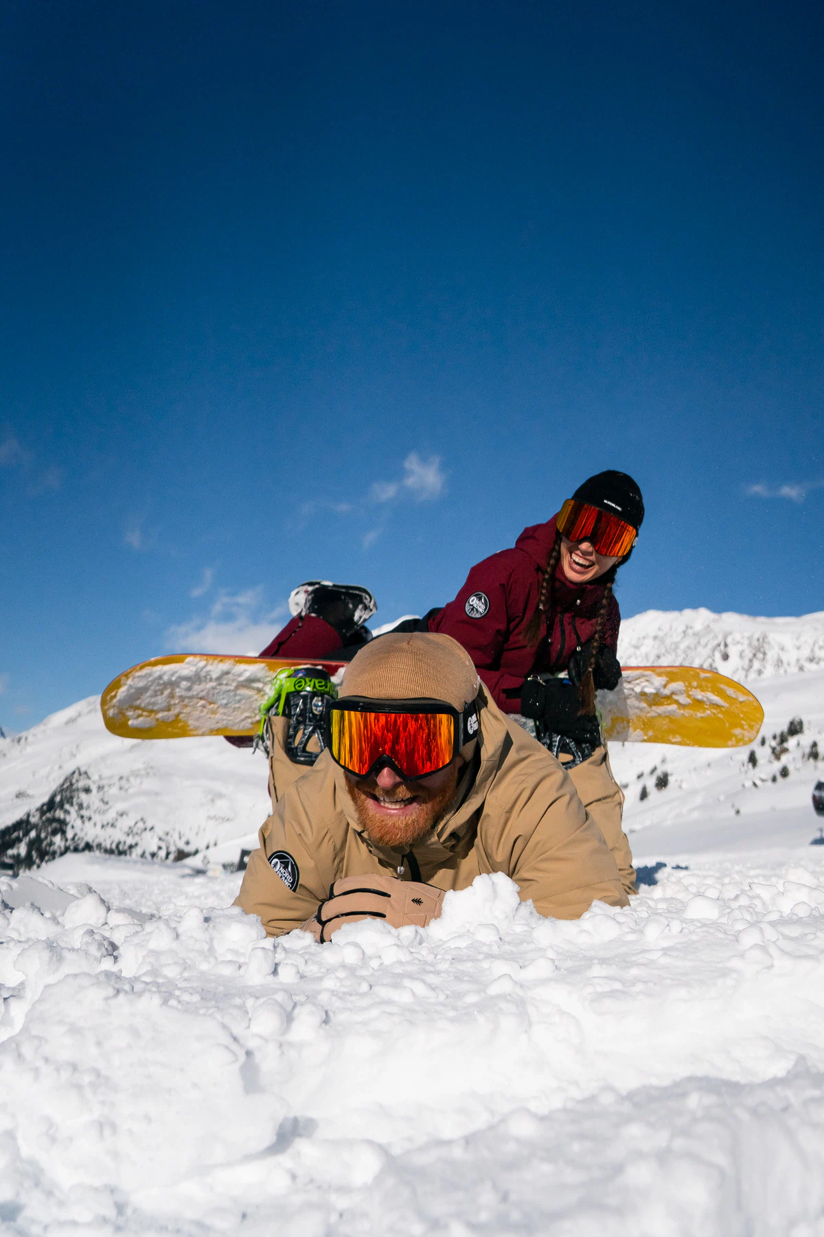 Snowboardisté v lyžařských brýlích leží ve sněhu pod modrou oblohou